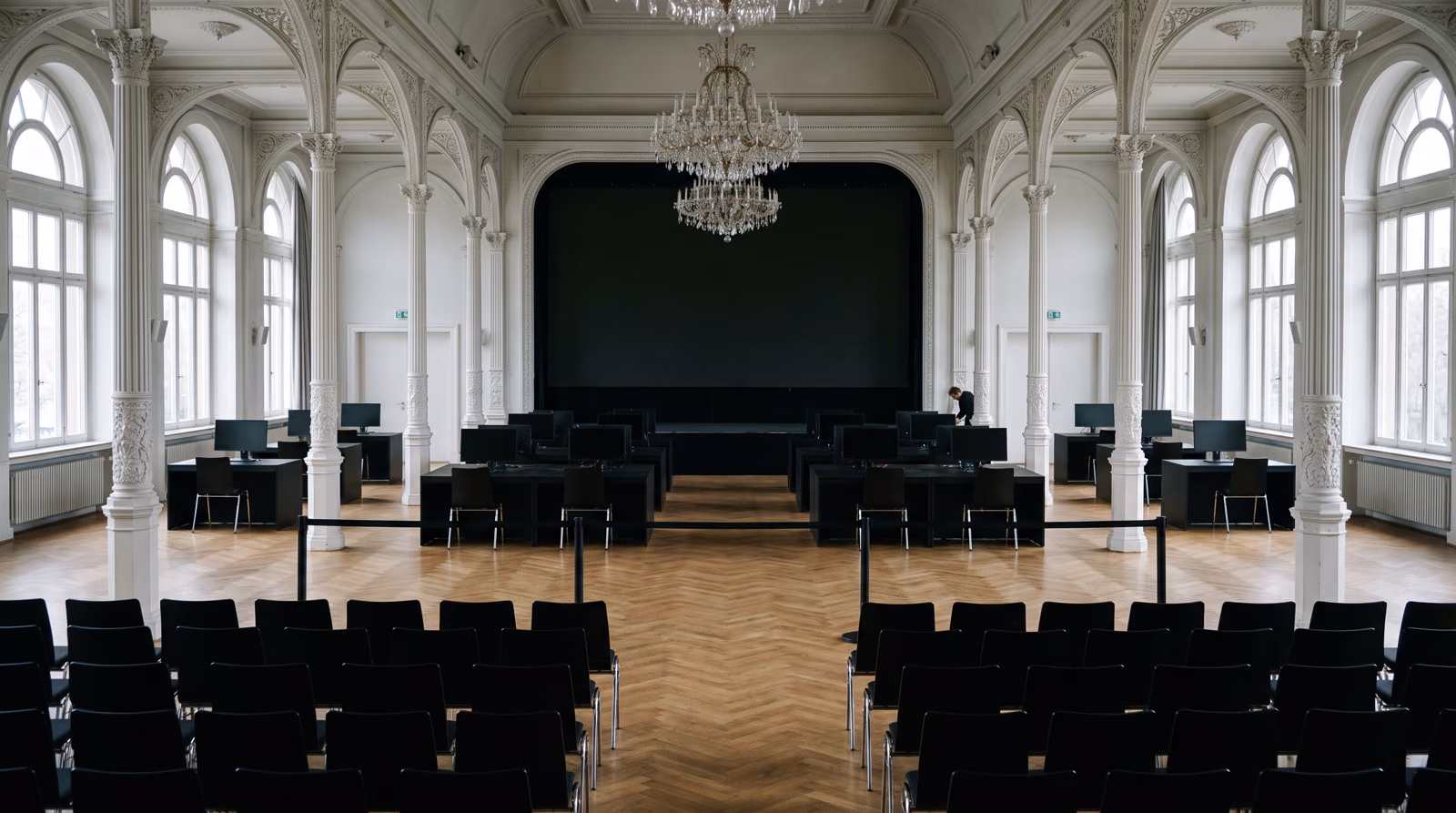 Der leere Festsaal der Flora am Morgen, Tageslicht durch die hohen Fenster: vorn die Stuhlreihen, hinten die zwölf Startplätze, Einzeltische und Teamtische, noch niemand sitzt. KI-Visualisierung des geplanten Tages. Basis: echtes Foto der Flora Köln.